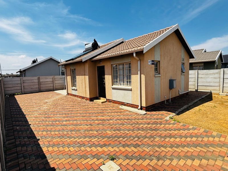 A detached single-story house featuring a paved driveway, precast boundary walls, and a solar water heating system on the tiled roof.
