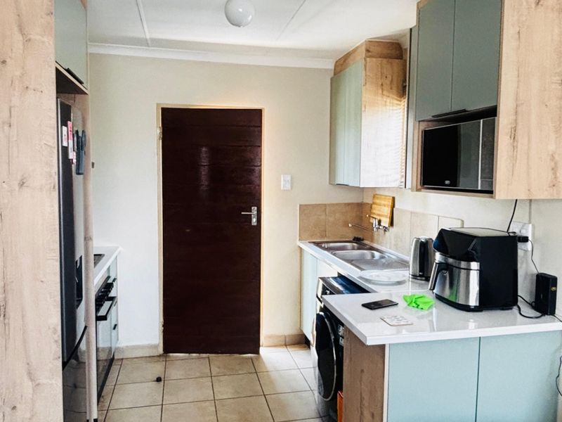 A functional kitchen featuring modern two-tone cabinetry, laminate countertops, tiled flooring, and integrated appliances, providing a clean and practical workspace.