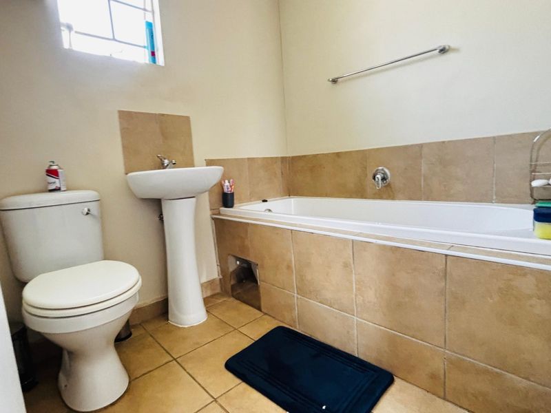 A functional bathroom featuring a pedestal washbasin, toilet, and a tiled built-in bathtub with a chrome towel rail.