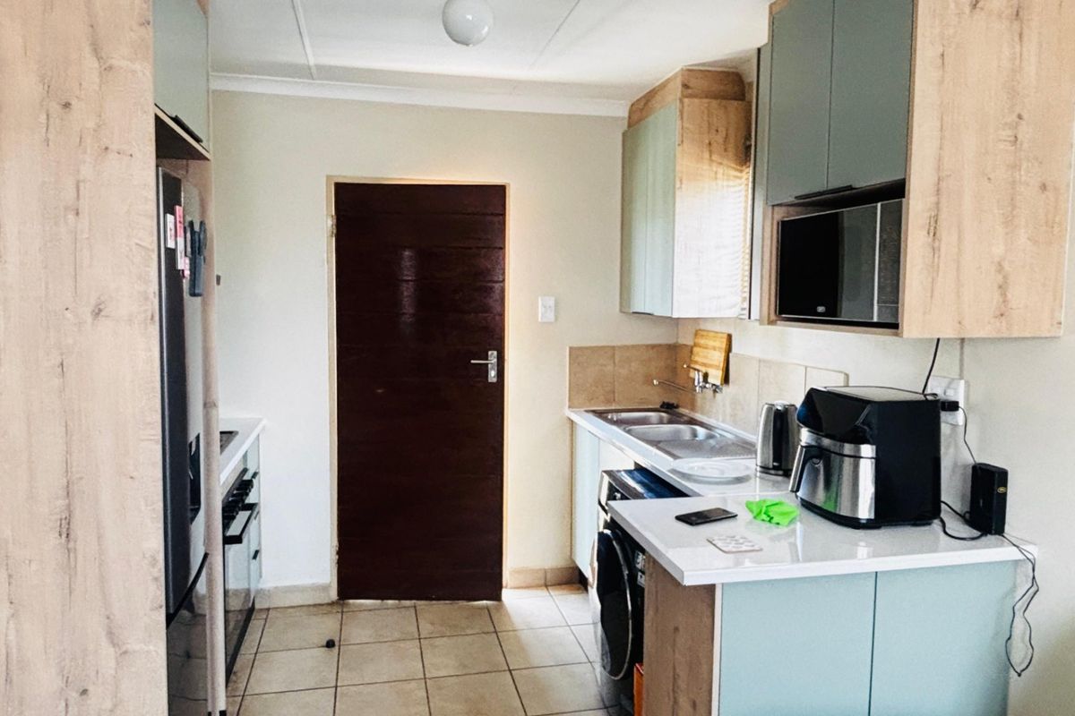 A functional kitchen featuring modern two-tone cabinetry, laminate countertops, tiled flooring, and integrated appliances, providing a clean and practical workspace.