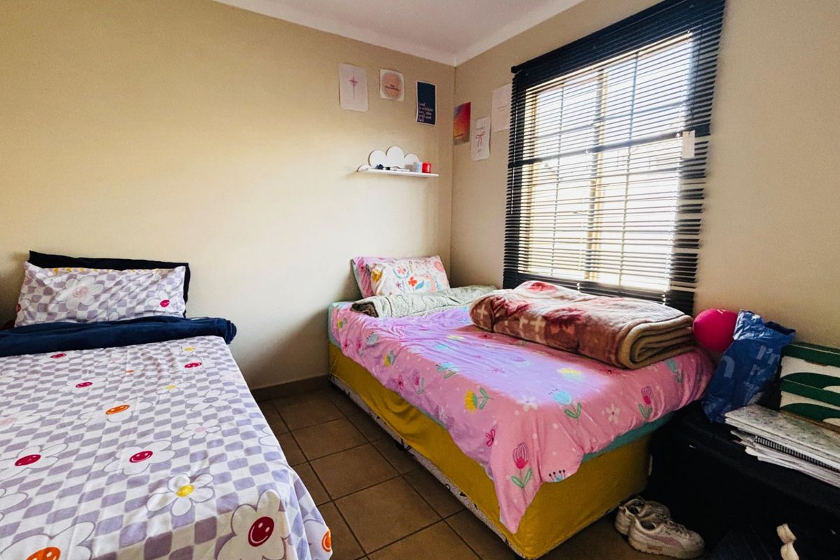 A functional bedroom featuring tiled flooring, a built-in wall shelf, and venetian blinds, providing a practical space for rest.