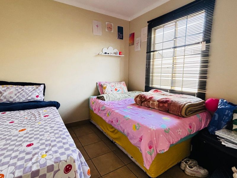 A functional bedroom featuring tiled flooring, a built-in wall shelf, and venetian blinds, providing a practical space for rest.