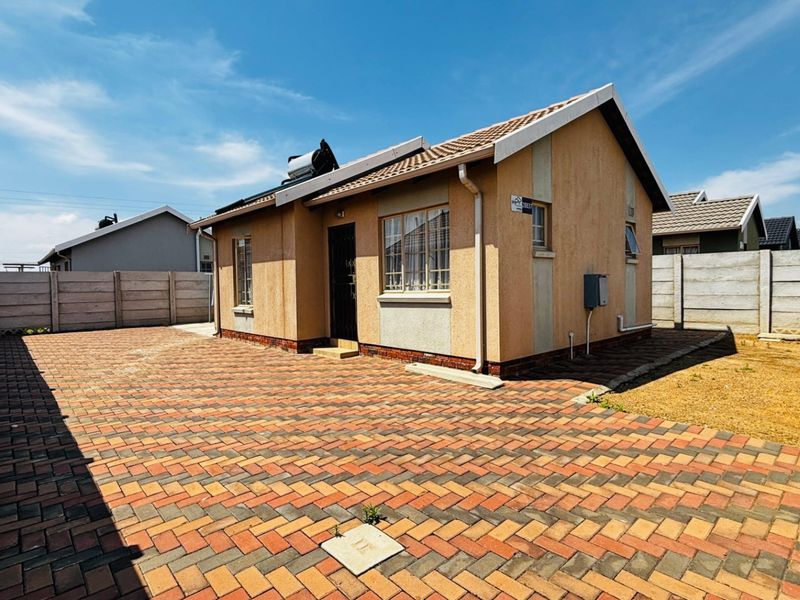 A well-maintained single-story house featuring a paved driveway, solar water heating system, and secure precast concrete boundary walls.