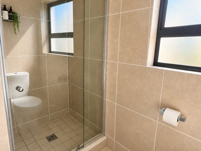 A modern bathroom featuring a glass-enclosed shower, neutral wall and floor tiling, and frosted glass windows for privacy.