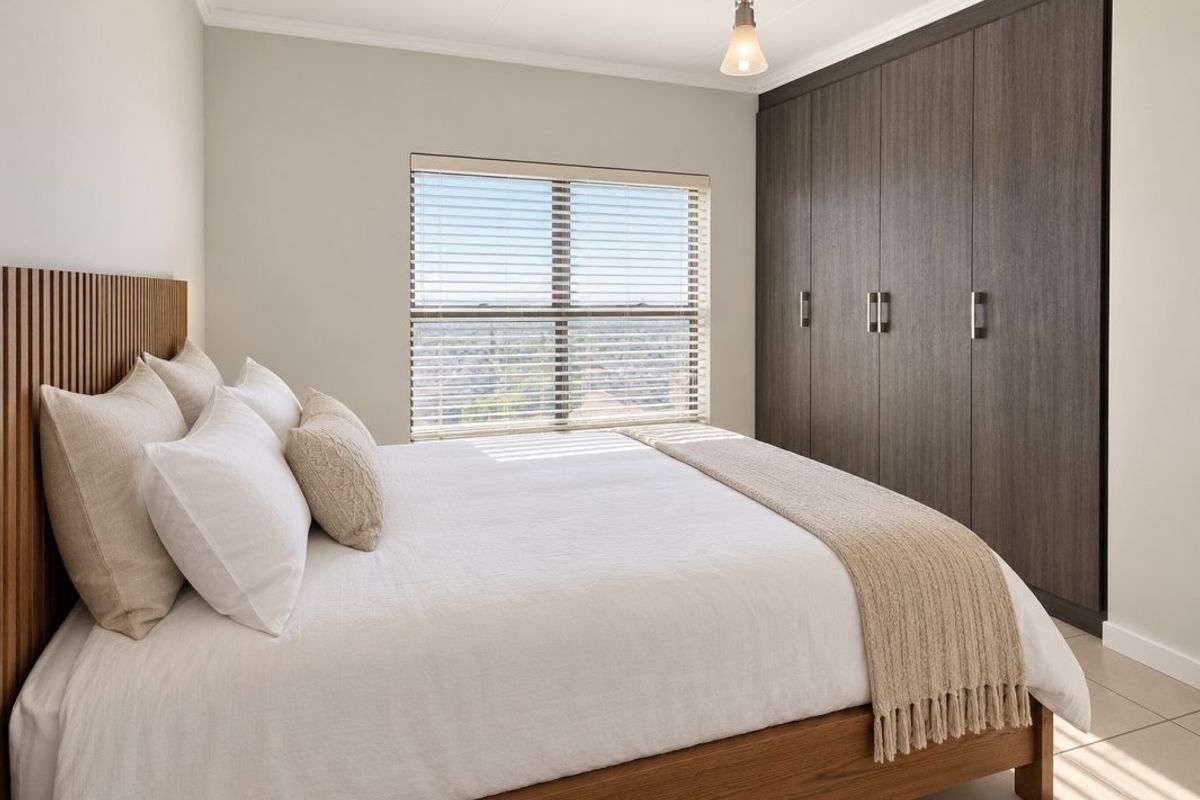 A well-maintained bedroom featuring dark wood built-in cupboards, tiled flooring, and a window with fitted venetian blinds.