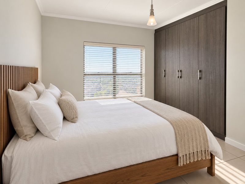 A well-maintained bedroom featuring dark wood built-in cupboards, tiled flooring, and a window with fitted venetian blinds.