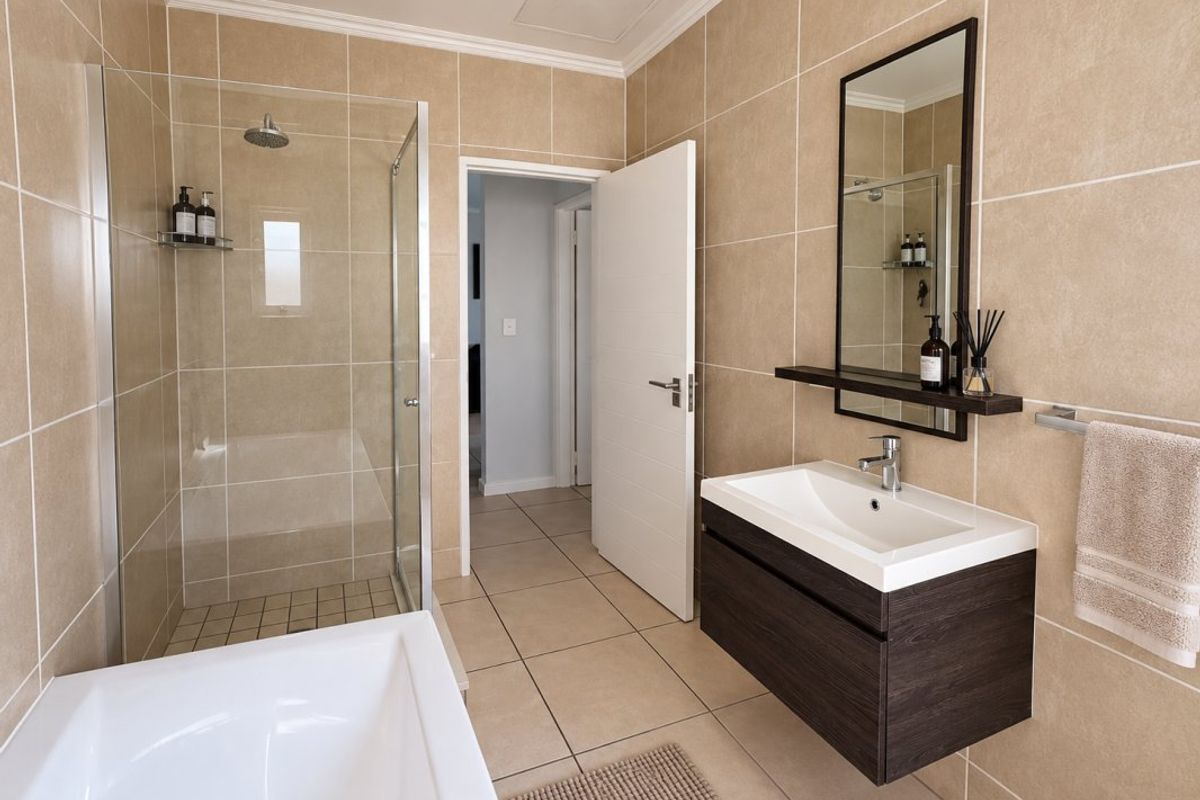 Modern bathroom featuring a glass-enclosed shower, a deep bathtub, and a sleek wall-mounted vanity with a basin and mirror.