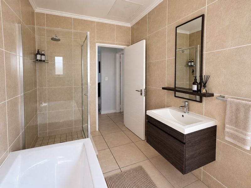 Modern bathroom featuring a glass-enclosed shower, a deep bathtub, and a sleek wall-mounted vanity with a basin and mirror.
