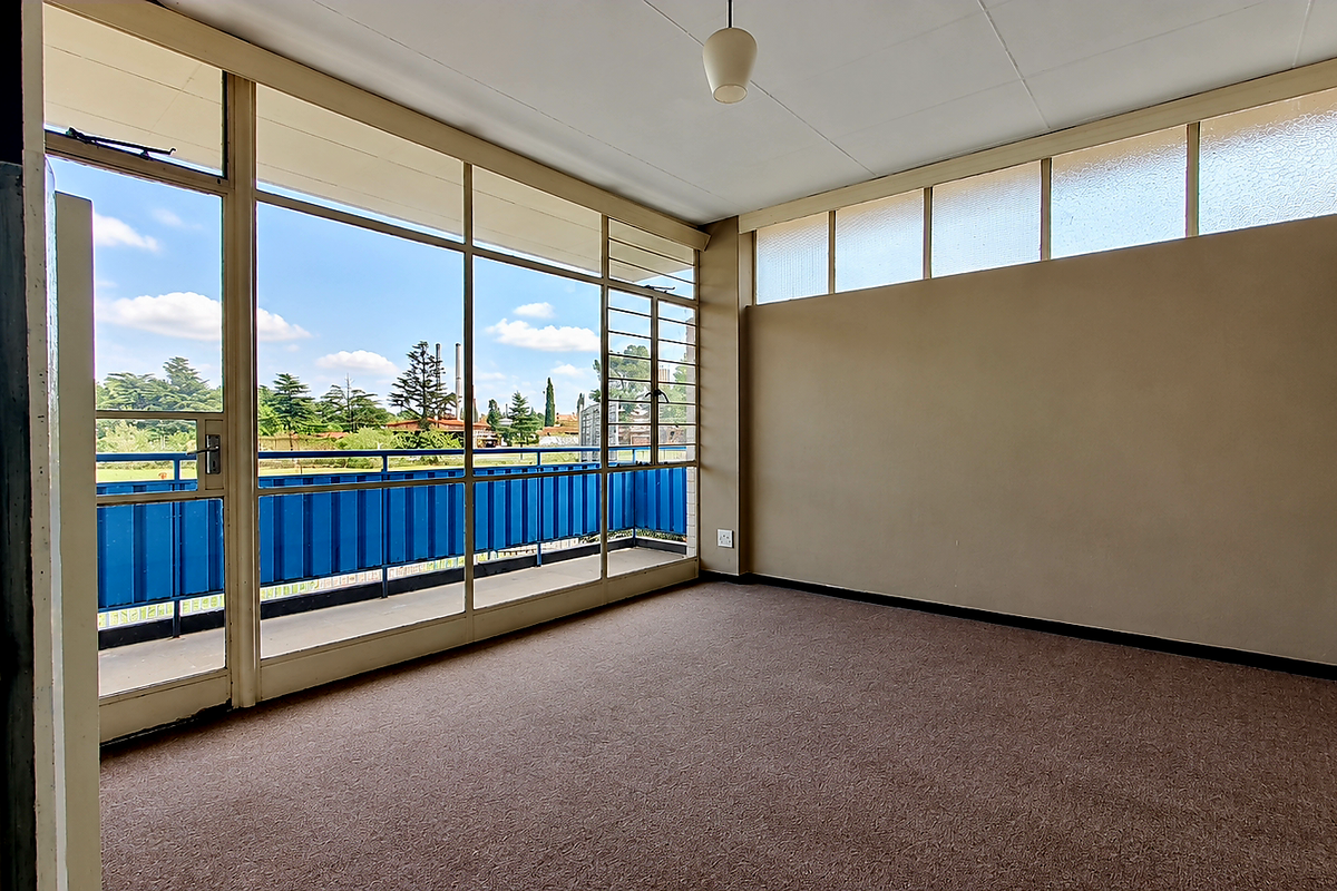 A bright, empty living area featuring expansive floor-to-ceiling windows, high-level clerestory windows, and direct access to a private balcony.