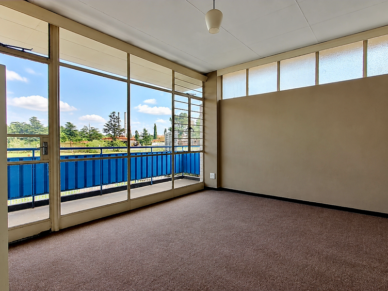 A bright, empty living area featuring expansive floor-to-ceiling windows, high-level clerestory windows, and direct access to a private balcony.