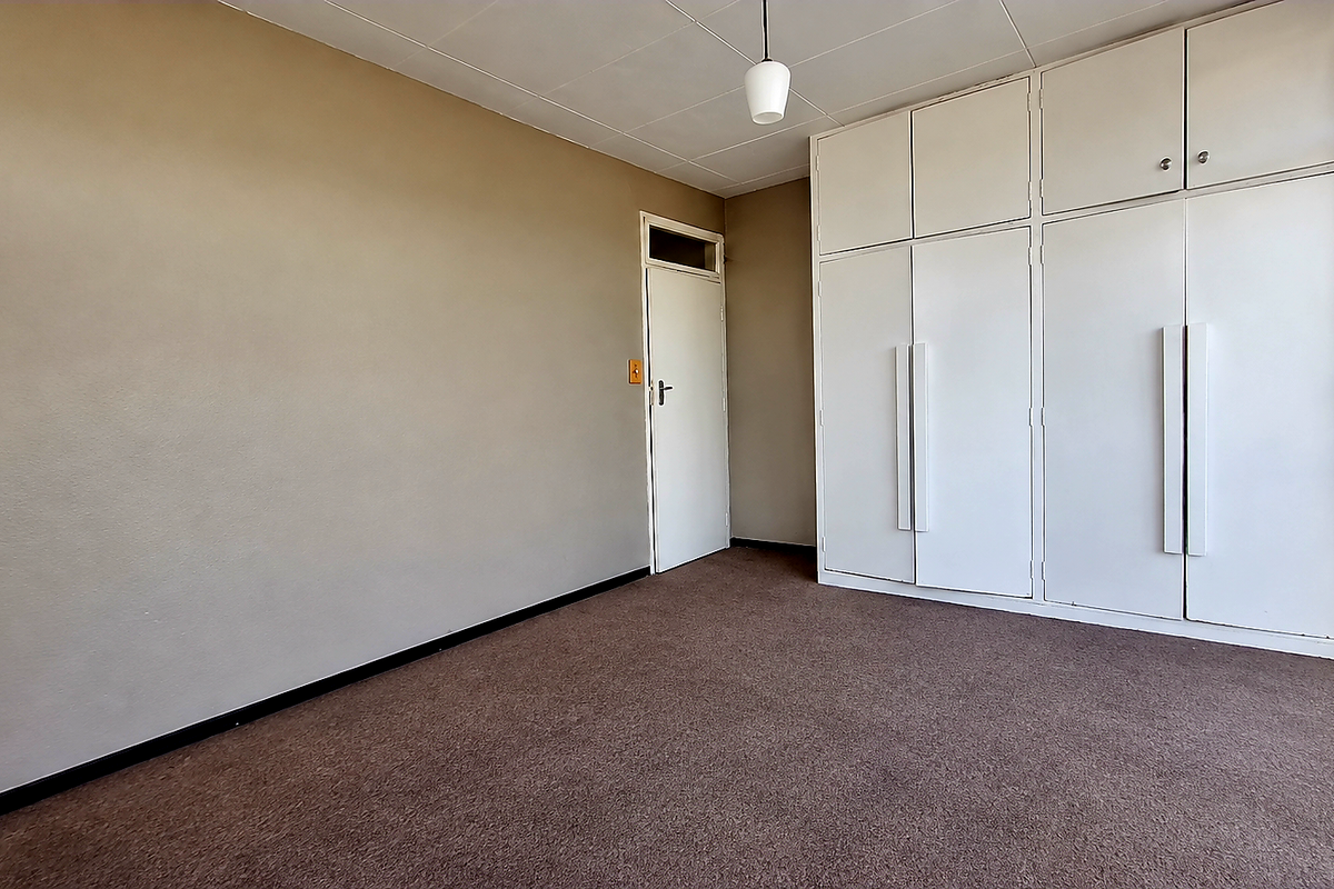 A spacious, empty bedroom featuring neutral wall tones, carpeted flooring, and extensive built-in cupboard storage with overhead cabinetry.