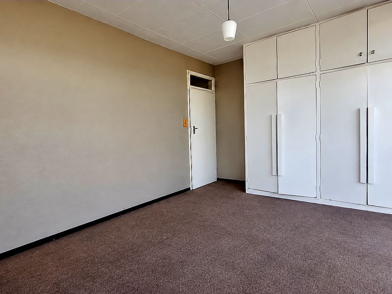 A spacious, empty bedroom featuring neutral wall tones, carpeted flooring, and extensive built-in cupboard storage with overhead cabinetry.
