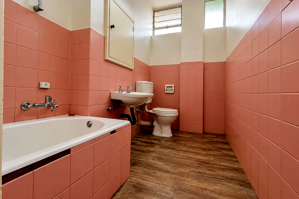 A dated bathroom featuring pink wall tiles, a standard bathtub, pedestal basin, and toilet, with louvered windows providing natural ventilation.