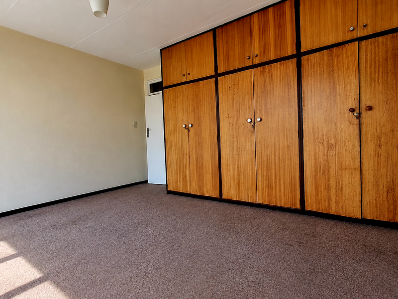 An empty bedroom featuring wall-to-wall built-in wooden cupboards and carpeted flooring, offering a blank canvas for potential updates.