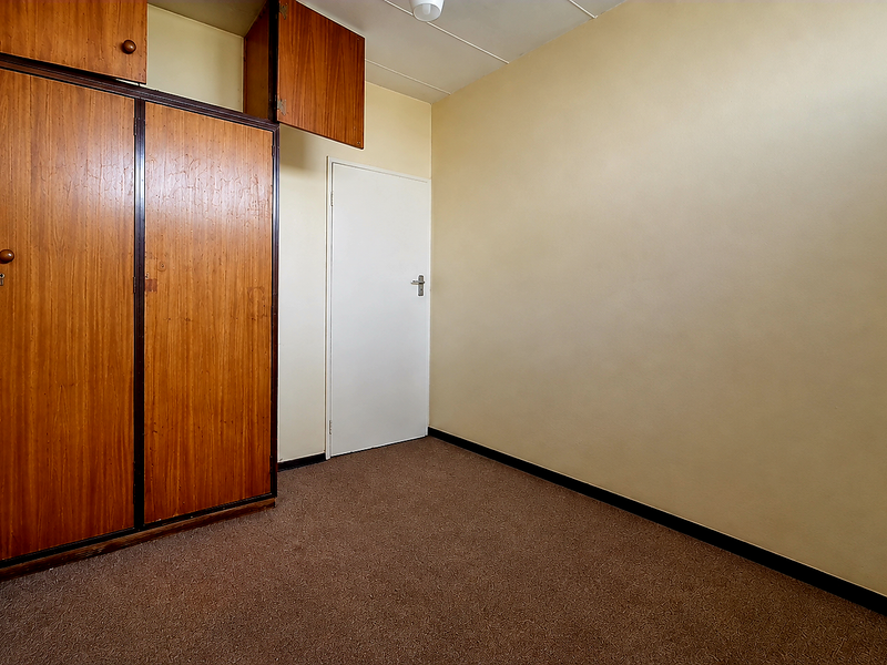 An empty bedroom featuring built-in wooden cupboards and carpeted flooring, offering a blank canvas for renovation or restyling.