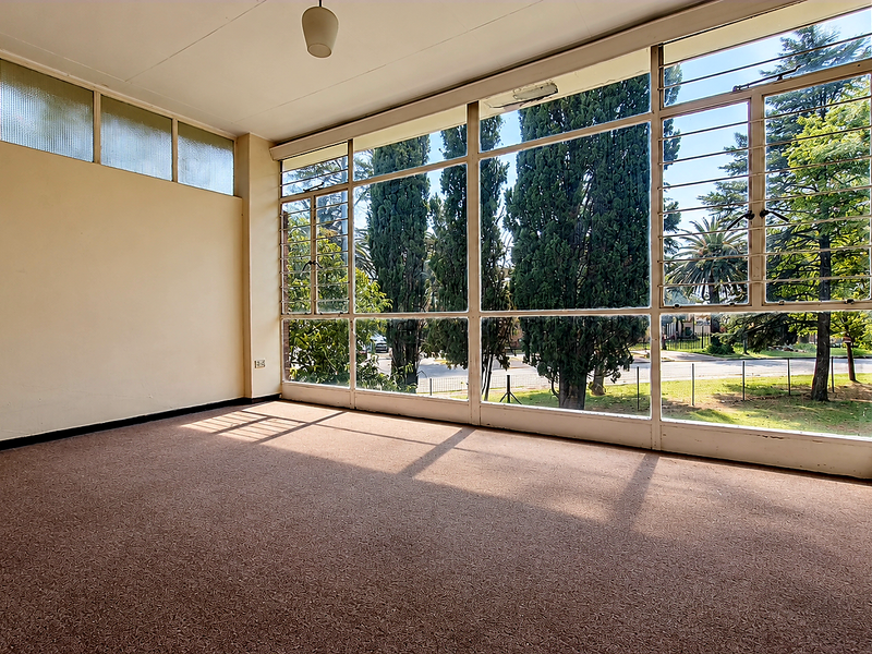 A bright, empty living room featuring expansive steel-framed windows that provide ample natural light and views of the surrounding greenery.
