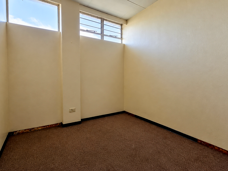 An empty bedroom featuring high-level windows, carpet flooring, and neutral walls, offering a blank canvas for potential renovation or interior design updates.