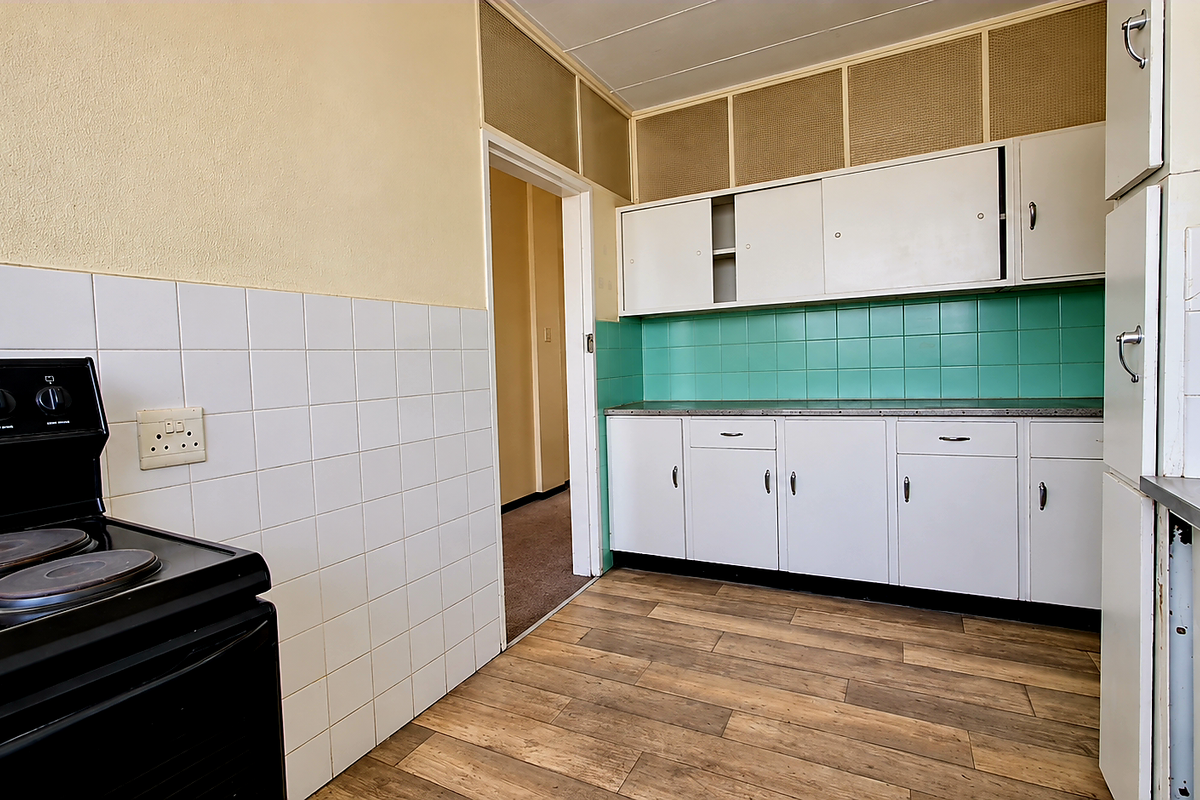 A dated kitchen featuring white cabinetry, green tiled backsplash, and an electric stove, offering a functional layout ready for modernization.