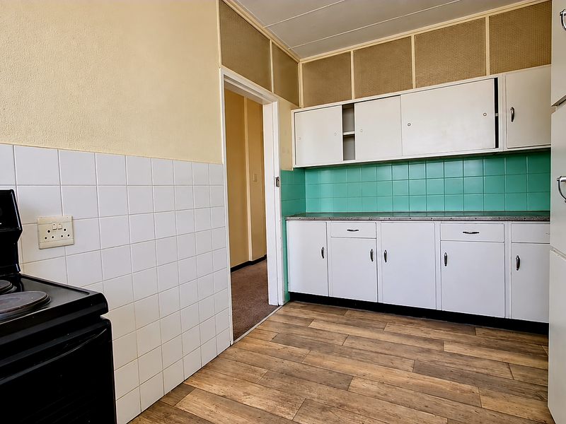 A dated kitchen featuring white cabinetry, green tiled backsplash, and an electric stove, offering a functional layout ready for modernization.