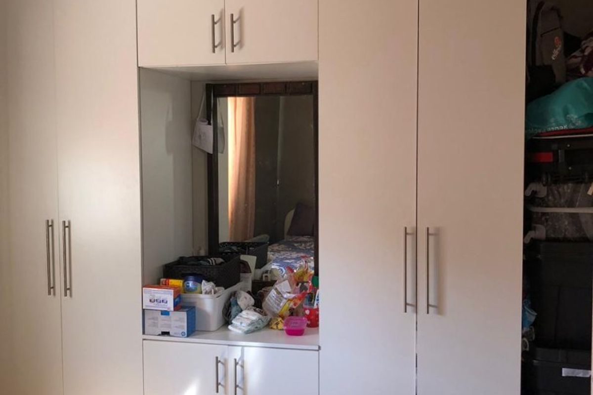 A bedroom featuring a large, white built-in wardrobe with integrated vanity mirror and tiled flooring.