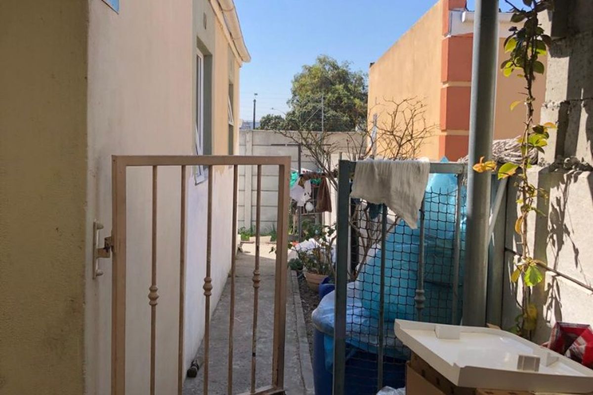 A narrow side passage or rear exterior area featuring a metal security gate, concrete pathway, and perimeter walling.