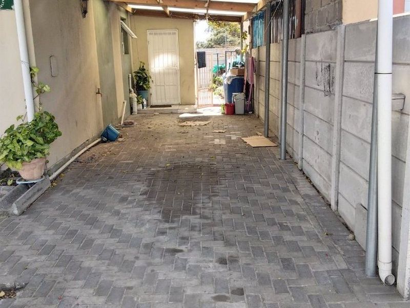 A covered outdoor paved area featuring a corrugated metal roof and precast concrete boundary wall, suitable for use as a carport or utility space.