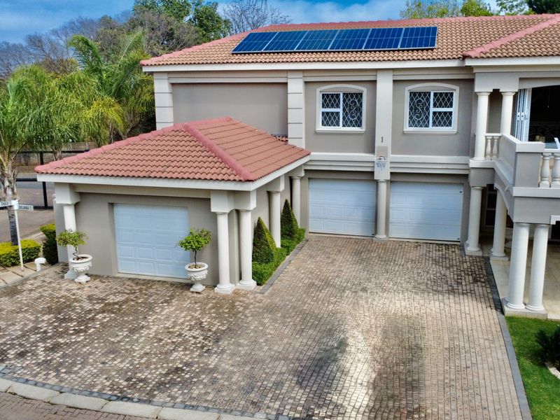 Aerial view of a multi-story house featuring a triple garage, paved driveway, balcony, and roof-mounted solar panels.