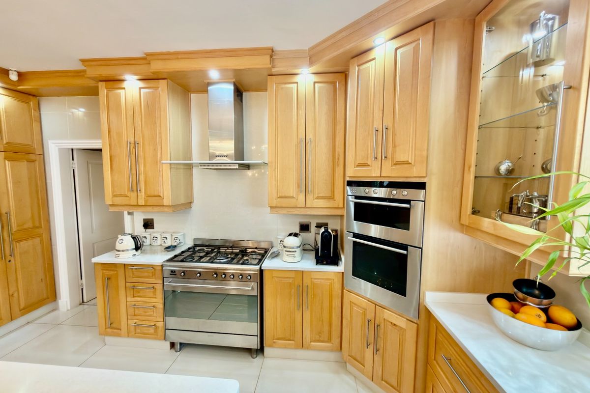 A well-maintained kitchen featuring light wood cabinetry, stainless steel appliances including a gas stove and double oven, and polished tiled flooring.