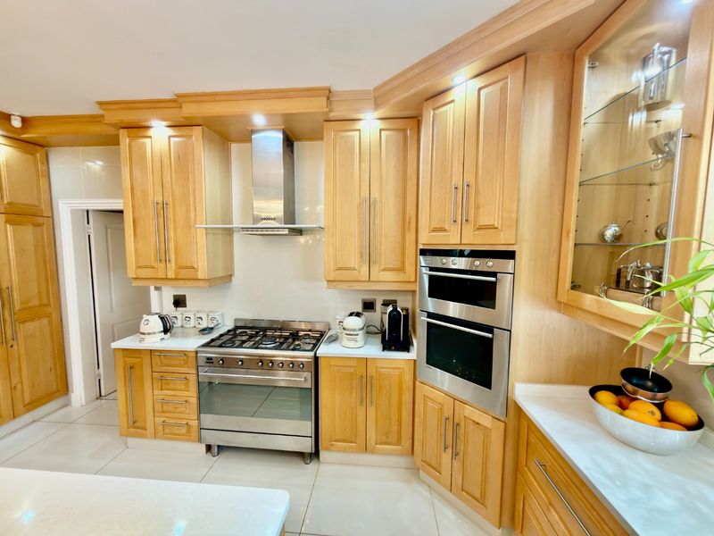 A well-maintained kitchen featuring light wood cabinetry, stainless steel appliances including a gas stove and double oven, and polished tiled flooring.