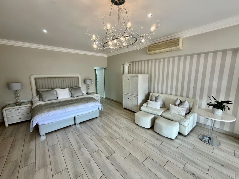 Spacious bedroom featuring wood-look tile flooring, a decorative chandelier, and a wall-mounted air conditioning unit with a striped wallpaper feature wall.