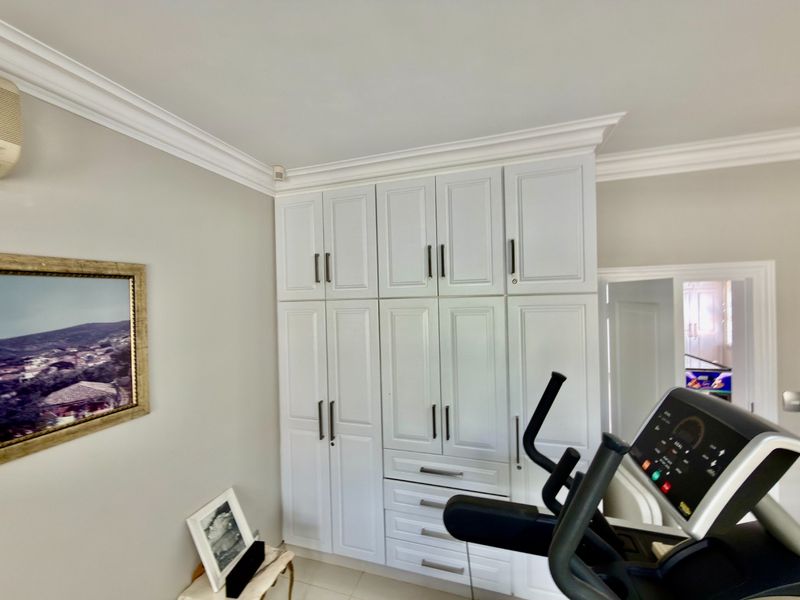 A bedroom featuring extensive white built-in cabinetry with modern hardware, crown molding, and a wall-mounted air conditioning unit.