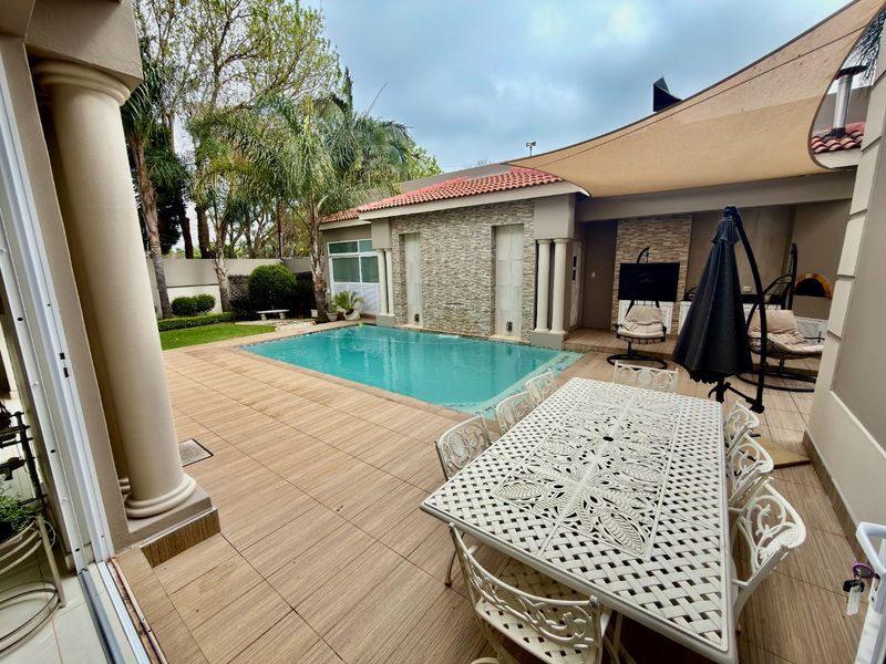 Outdoor entertainment area featuring a swimming pool, stone-clad feature wall, tiled patio, and a built-in pizza oven under a shade sail.