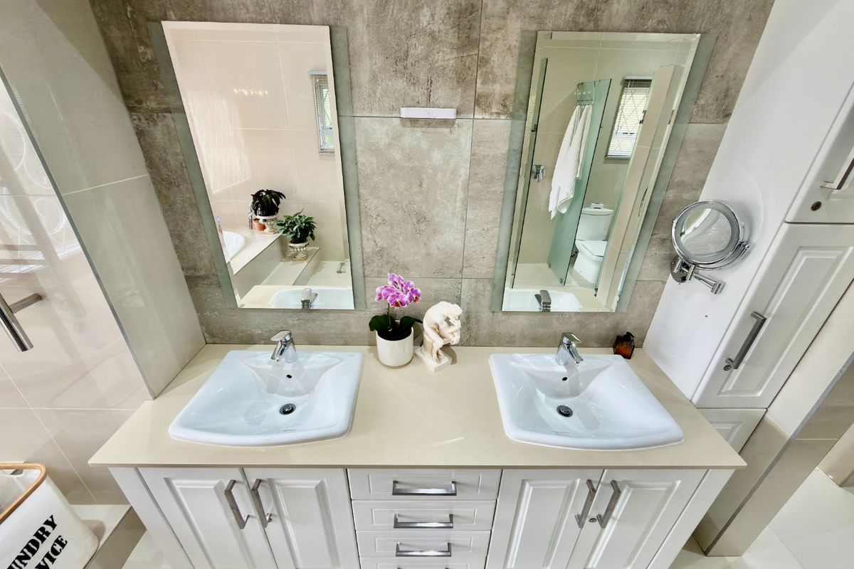 Modern bathroom featuring a double vanity with dual ceramic basins, stone countertop, ample built-in cabinetry, and large wall-mounted mirrors with tiled finishes.