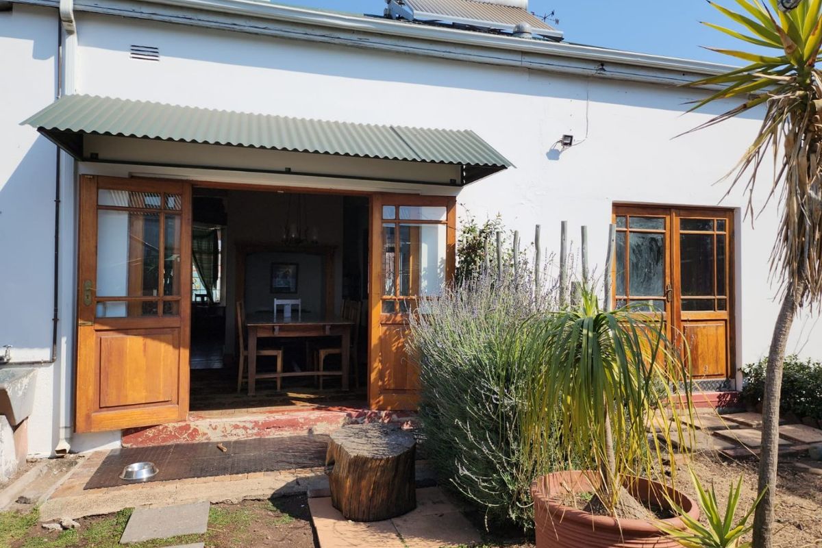 Rear exterior view of the house featuring timber french doors, a corrugated metal awning, and a roof-mounted solar water heater.