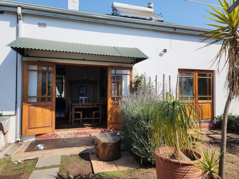 Rear exterior view of the house featuring timber french doors, a corrugated metal awning, and a roof-mounted solar water heater.
