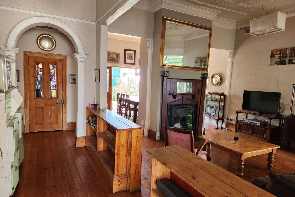 Spacious living room featuring original hardwood floors, ornate ceiling detailing, a classic fireplace with mantel, and an elegant arched entryway.
