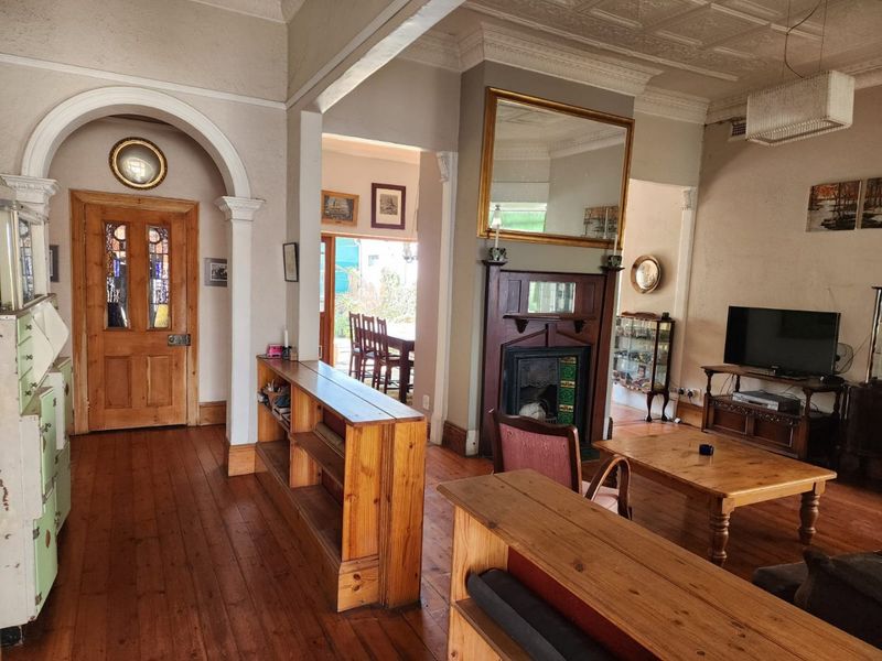 Spacious living room featuring original hardwood floors, ornate ceiling detailing, a classic fireplace with mantel, and an elegant arched entryway.