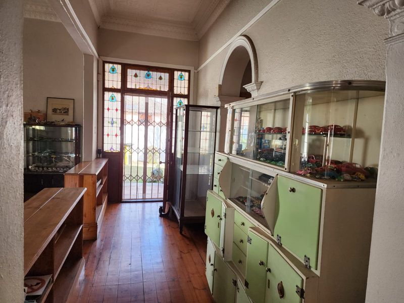 Welcoming entrance hall featuring original hardwood flooring, ornate ceiling cornices, and a characterful stained glass front door with security gate.