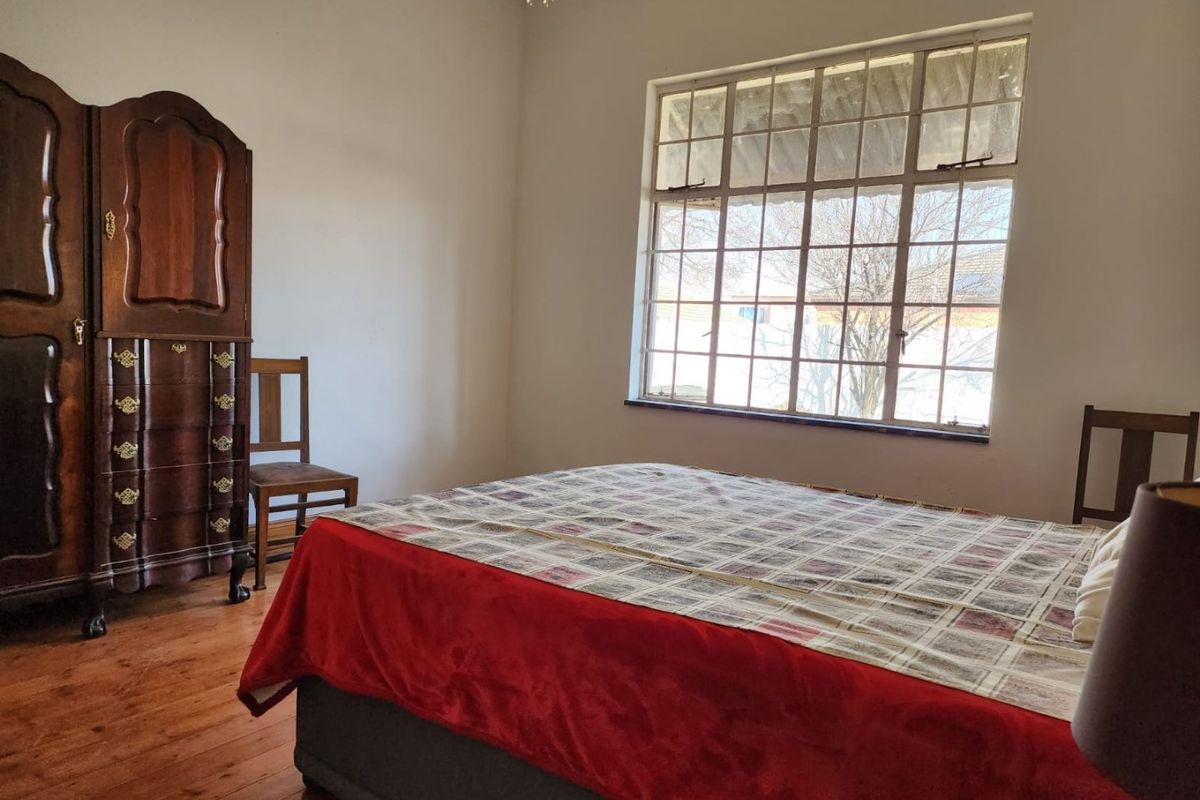 A bedroom featuring original timber flooring and a large multi-pane window, offering a classic aesthetic with potential for modern updates.
