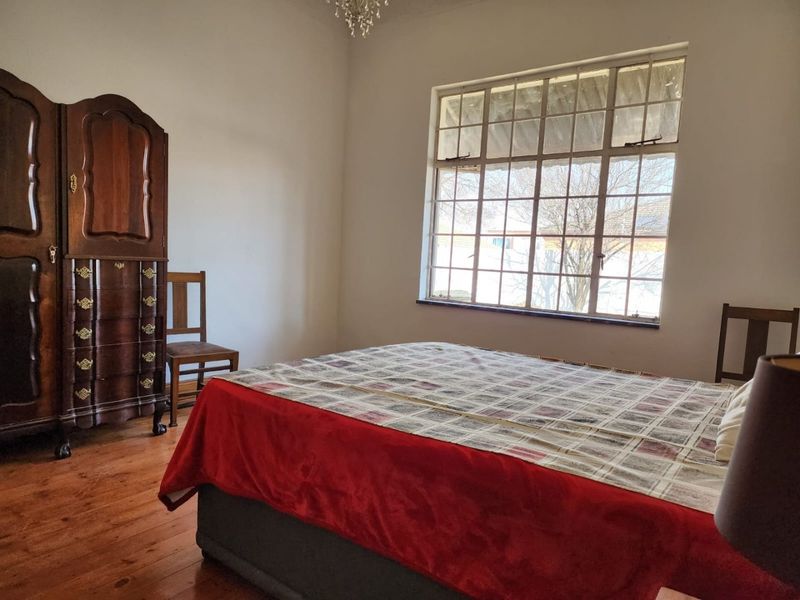 A bedroom featuring original timber flooring and a large multi-pane window, offering a classic aesthetic with potential for modern updates.