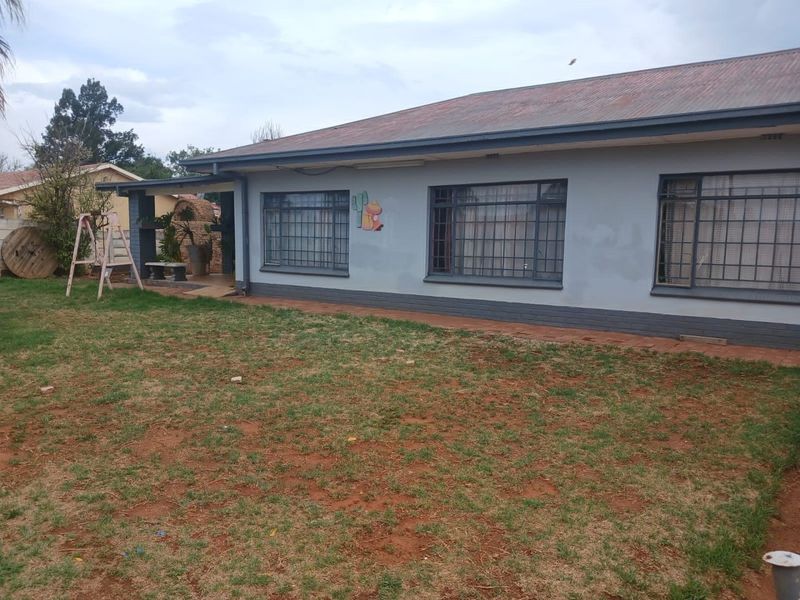 Rear view of the house featuring a corrugated metal roof, security bars on windows, and a small brick patio area with a built-in braai.