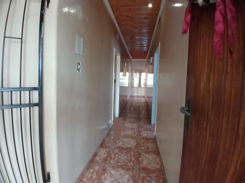 A long residential hallway featuring tiled flooring and a timber-paneled ceiling with recessed lighting.