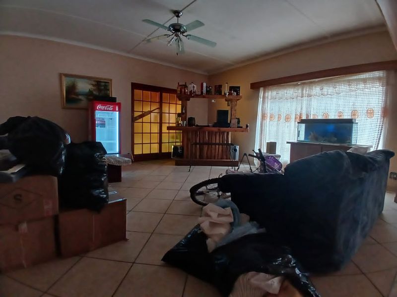 Spacious living area featuring tiled flooring, a ceiling fan, and a built-in bar, offering potential for a comfortable entertainment space.