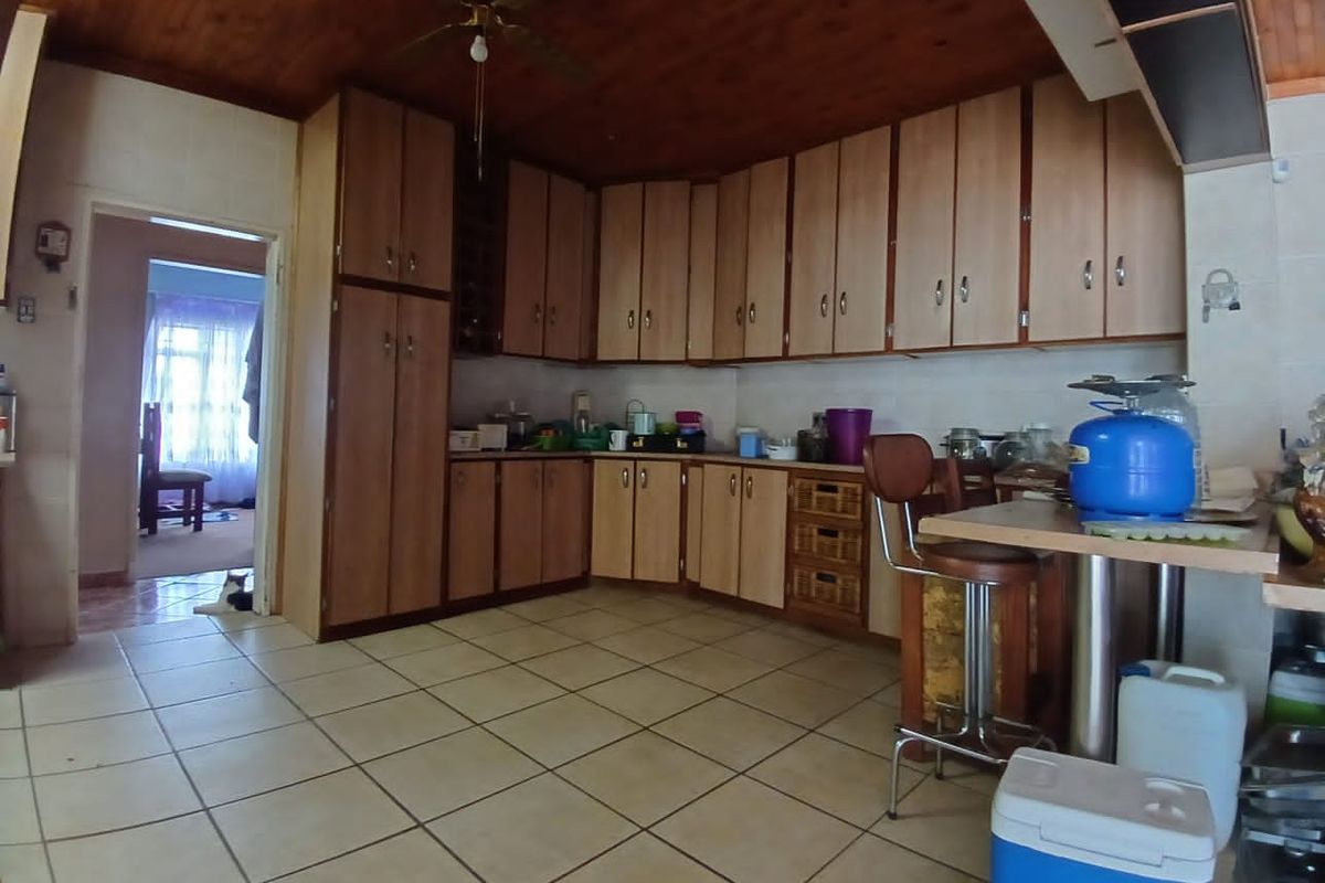 A dated kitchen featuring extensive built-in cabinetry, tiled flooring, and a timber-clad ceiling with an integrated fan.