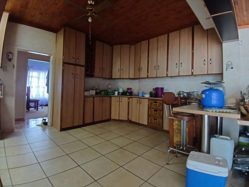 A dated kitchen featuring extensive built-in cabinetry, tiled flooring, and a timber-clad ceiling with an integrated fan.