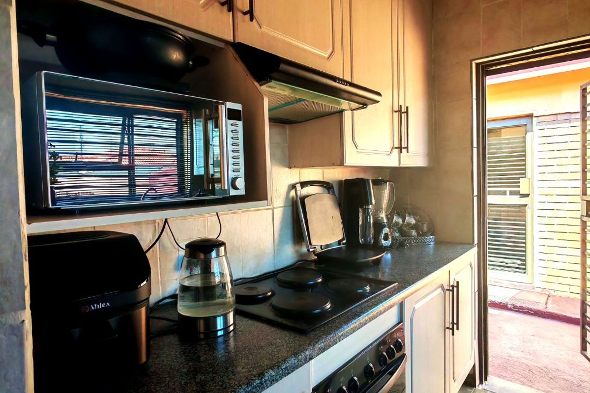 A functional kitchen featuring built-in cabinetry, granite countertops, an electric hob, and an integrated oven, with direct access to an outdoor area.