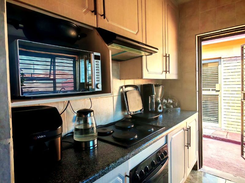 A functional kitchen featuring built-in cabinetry, granite countertops, an electric hob, and an integrated oven, with direct access to an outdoor area.