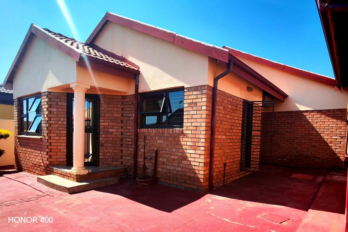 Rear exterior view of a face brick house featuring a paved patio area, security gates, and aluminium window frames.