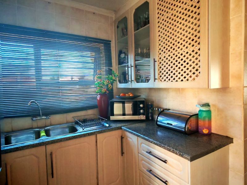 A functional kitchen area featuring light-toned cabinetry, dark laminate countertops, a double basin sink, and tiled backsplash with a window view.