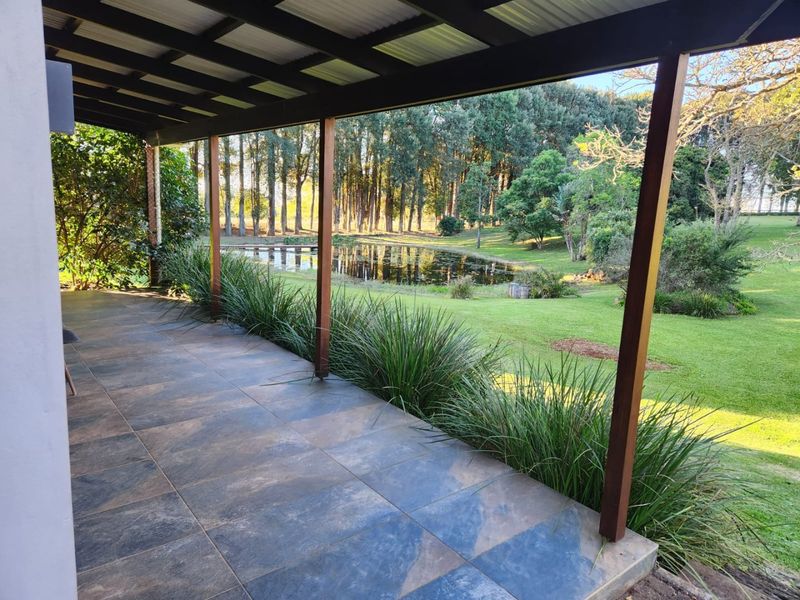 A spacious covered patio featuring tiled flooring and timber support posts, offering scenic views of the surrounding garden and pond.